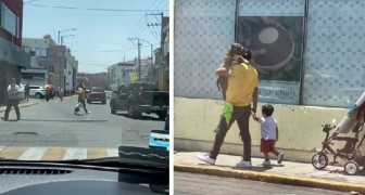 Man walks along the street with his dog in his arms like a baby, while his little son walks alongside