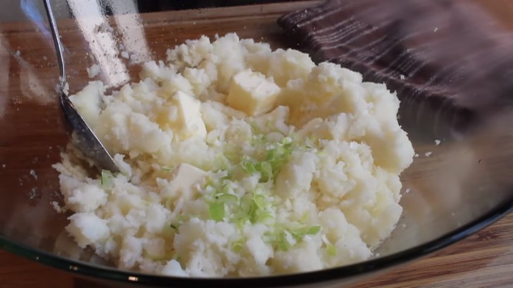 Meng de binnenkant van de aardappels in een kom met een paar blokjes boter en verse bieslook.