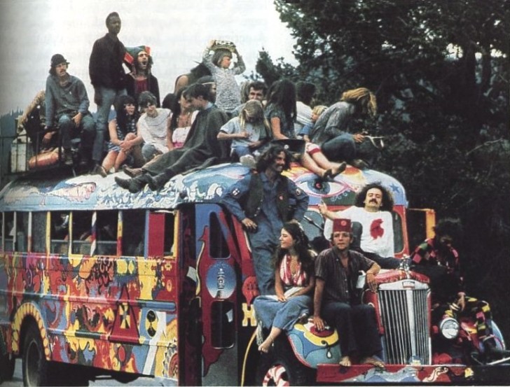 Een grote groep hippies op een oude schoolbus.