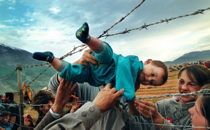 1. I membri di una famiglia in Kosovo affidano il piccolo Agim Shala di 2 anni ai nonni in un campo in Albania attraverso una barriera di filo spinato (Marzo 1999).