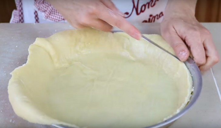Flatten the pastry dough with a rolling pin and place it in a greased and floured pan; remove excess edges of the dough.