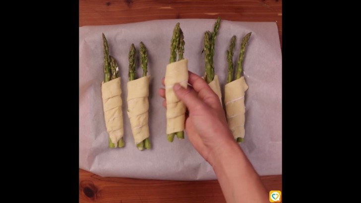 Disposez les asperges sur le papier de cuisson, badigeonnez la pâte avec le jaune d’œuf et saupoudrez la surface avec le parmesan.