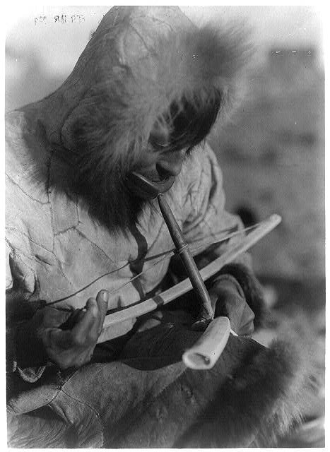 12. Un homme esquimau sculptant une défense en ivoire à la main.