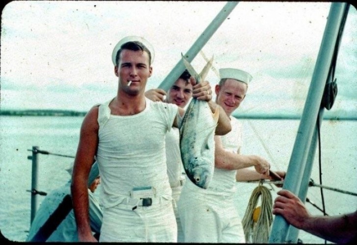 Min farfar på 50-talet håller en fisk, röker cigaretter och har en bok innanför midjan och förpackningen i ärmen.