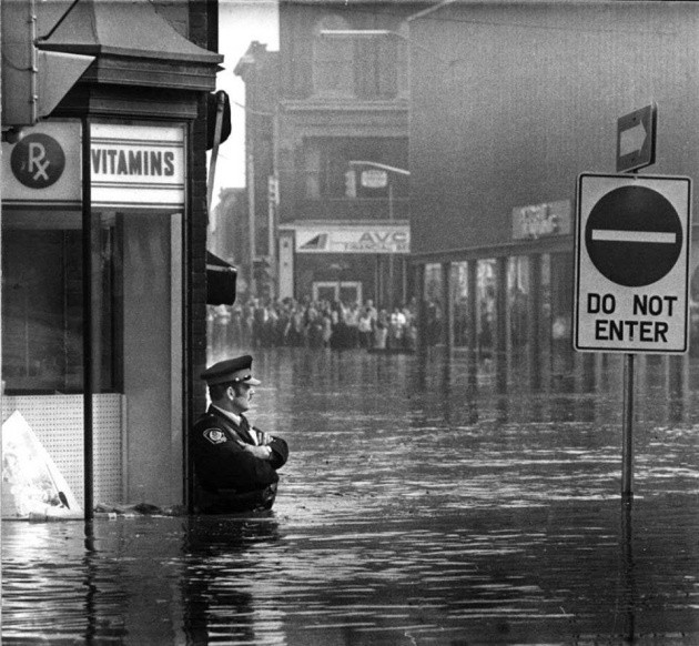 18. Un poliziotto tiene di guardia l'entrata della farmacia dopo l'alluvione che colpì l'Ontario, nel 1974.