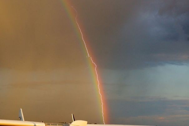 Bliksemschicht gaat door een vliegtuig heen op het moment dat deze laatste door een regenboog gaat.