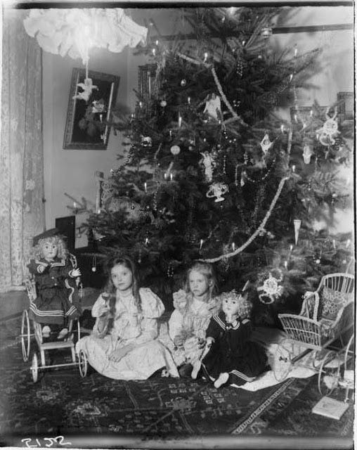 Deux filles posent au pied de l'arbre avec des poupées reçues pour Noël.