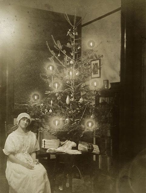 Une femme assise à côté d'un sapin de Noël décoré de (vraies) bougies.