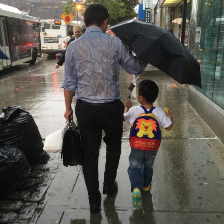 Questo padre lascia che la pioggia lo bagni completamente, pur di coprire il figlio con l'unico ombrello.
