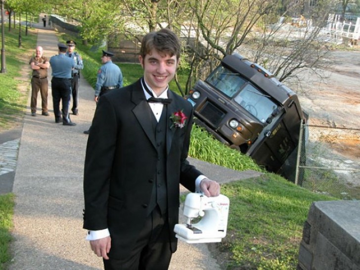 18. Un jeune homme vêtu d'un costume élégant tenant une machine à coudre devant une camionnette qui s'est renversée . Tout est normal, non?