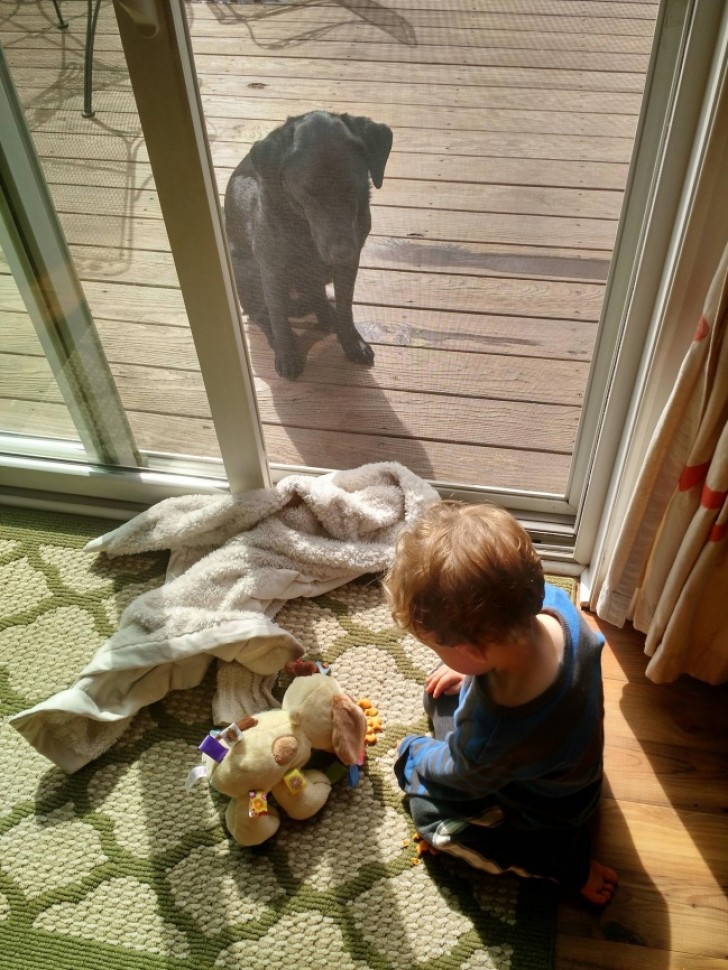 Mijn zoon die zijn denkbeeldige goudvis te eten geeft, terwijl zijn hond buiten wacht.