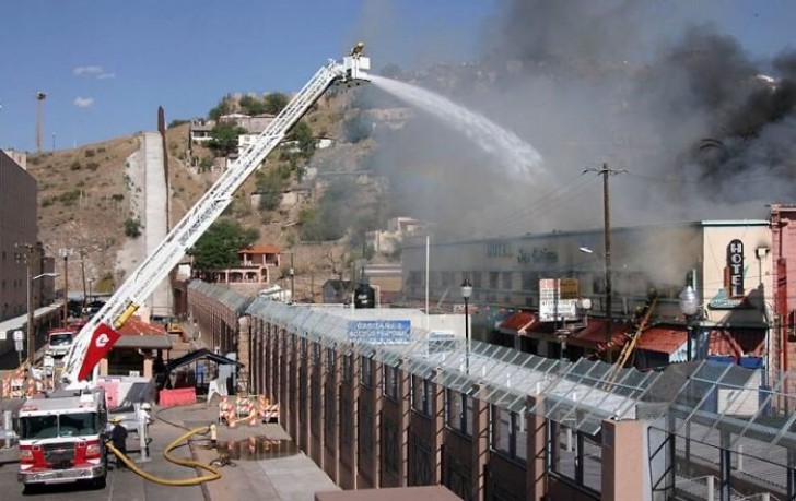 Een team van brandweerlieden in Arizona in actie om een brand in Mexico te blussen, voorbij de muur.