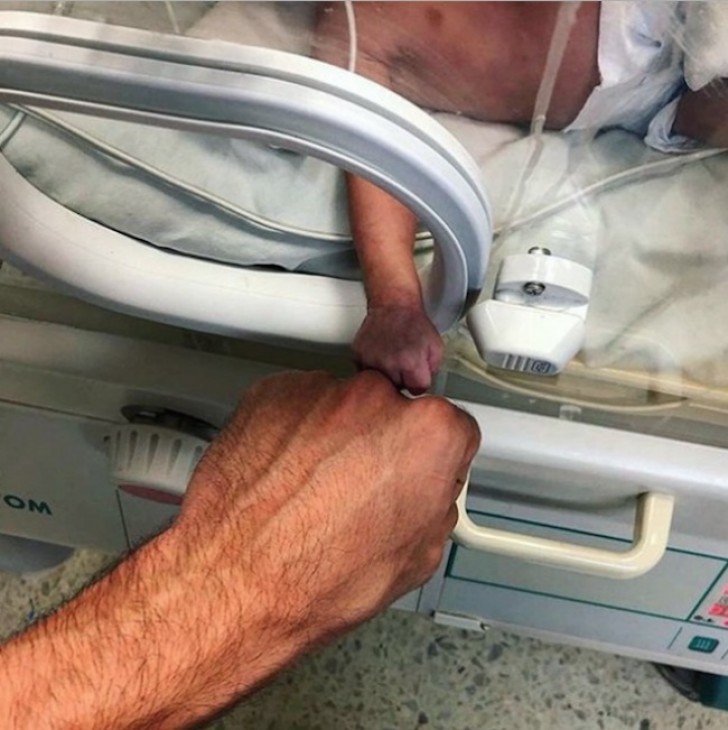 A dad and his premature child making a gesture that represents hope.