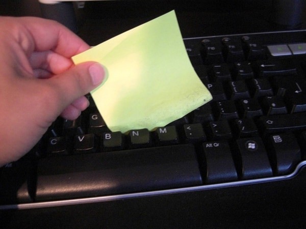 Mit einem Zettel mit Klebestreifen könnt ihr den Staub in einer Tastatur entfernen.