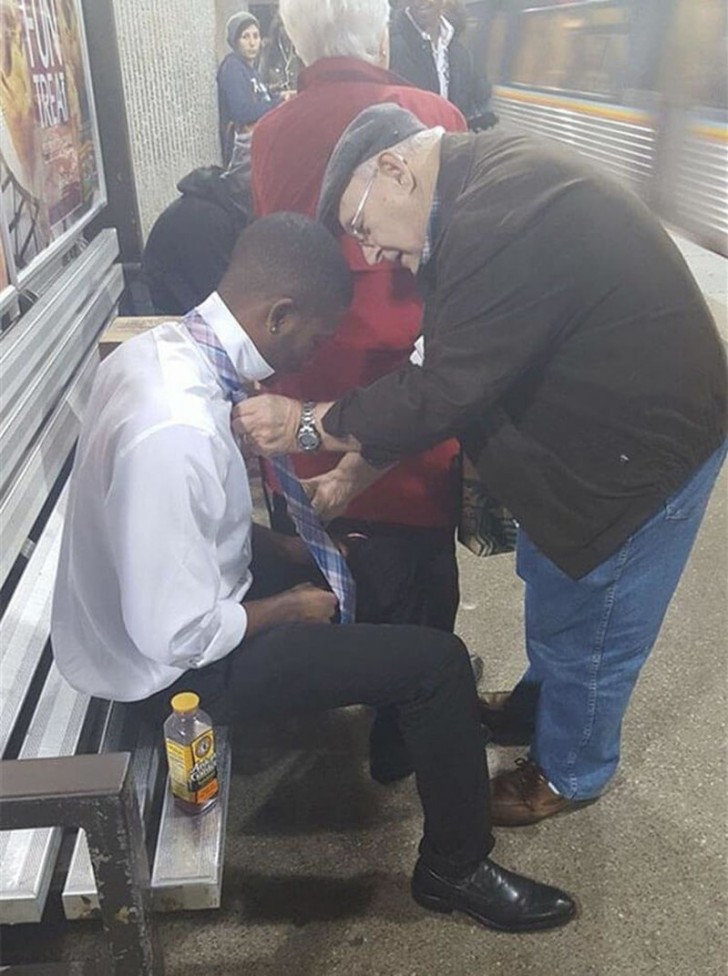 An elderly man helps a young man to tie his tie properly.