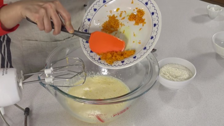 Wanneer je een witte creme hebt verkregen, voeg je de gesmolten boter toe, de helft van de sinaasappelschillen en de amandelbloem.