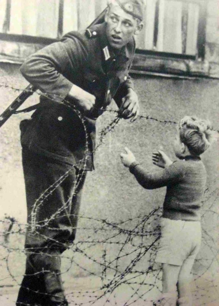 15. Un soldato aiuta un bambino ad oltrepassare il muro di Berlino.