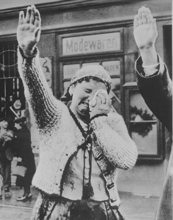 8. 1938: Eine Frau ist gezwungen, den triumphierenden Hitler zu begrüßen, kann aber ihre Verzweiflung nicht verbergen.