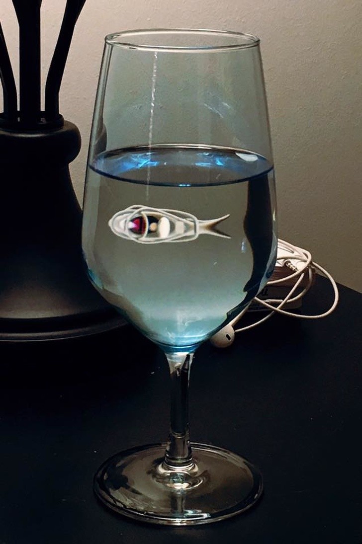 Un pesce con le cuffie ascolta musica sotto l'acqua contenuta in un bicchiere. Poetico, no?