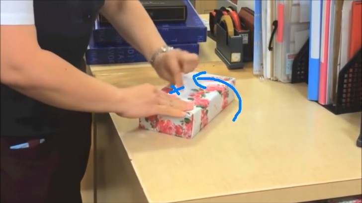 6. Sollevate il lembo di carta in alto e posatelo sul regalo, facendo attenzione a ripiegare in sotto il bordo, in modo che non fuoriesca. Fermate con dello scotch dove vedete la 