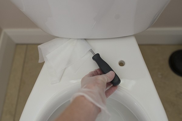 5. Pulire la fessura tra il sedile e il serbatoio del WC aiutandosi con un cacciavite coperto con una salvietta disinfettante
