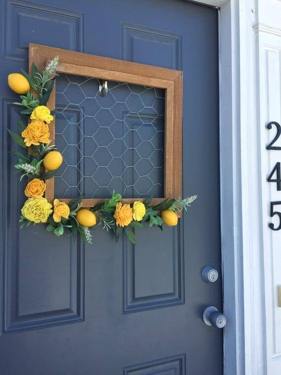 4. Ulteriore variante per la decorazione della porta di casa: una cornice con rete metallica, limoni e fiori gialli