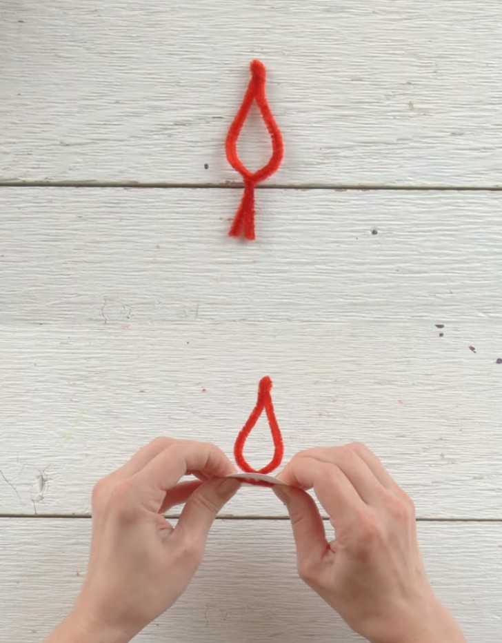 4. Modellate uno scovolino rosso a mo' di fiamma, tagliando le estremità e poi infilatelo in un cerchio di carta dello stesso diametro del tubo, fissandolo con della colla a caldo