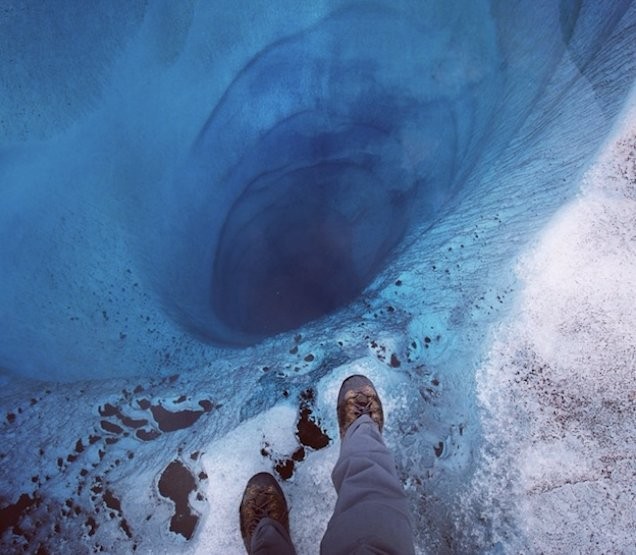 Un alpiniste au bord d'une fissure très profonde dans la glace.