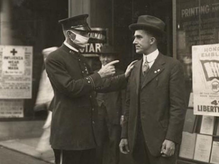 1. Ein Polizist in San Francisco, der damit beschäftigt ist, einen Mann auf der Straße zurechtzuweisen, der trotz der Grippe-Pandemie von 1918 keine Maske trägt.