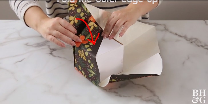 4. Faites remonter le rabat légèrement plié vers le cadeau, de façon à le ramener vers le dessus et à emballer la surface, en restant toujours à ras du paquet