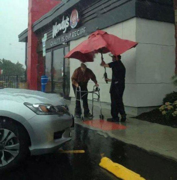 8. Der Ladenmitarbeiter nimmt den Schirm vom Tisch, um den älteren, gehbehinderten Mann vor dem Regen zu schützen.