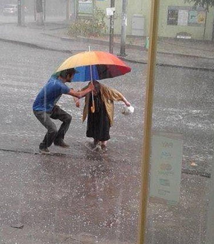 A simple gesture in helping an elderly lady cross the road, sheltering her from the rain