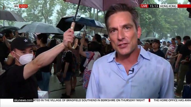 Ein pazifistischer Protestant hält einen Regenschirm über den Live-Reporter: eine sehr großzügige Geste!