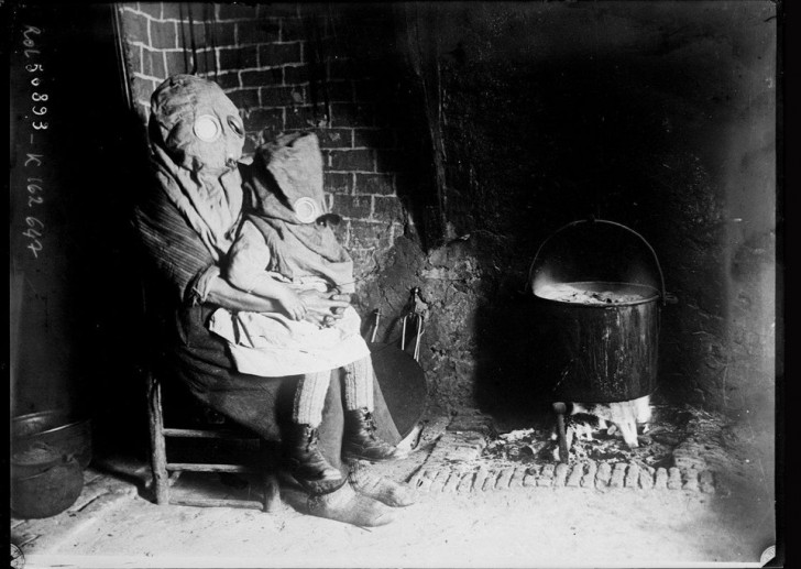 1918, France. Mère et fille photographiées portant un masque à gaz alors qu'elles se trouvent dans leur maison près de la cheminée