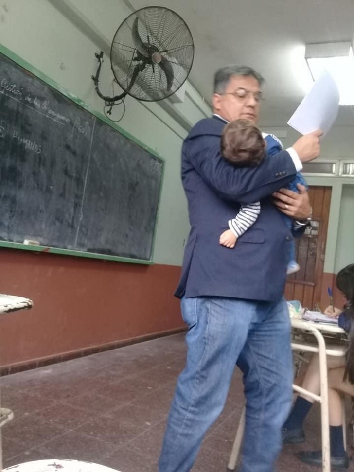 Profesor sostiene en sus brazos al hijo de una joven estudiante para que pueda seguir mejor la lección - 1