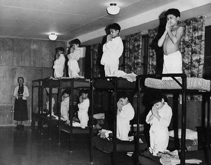 6. Das genaue Jahr ist nicht bekannt, man vermutet, dass das Foto zwischen 1930 und 1970 aufgenommen wurde. Indigene Kinder werden gezwungen, in der Einrichtung zu beten.