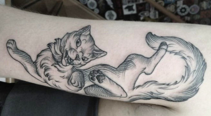 Tatuaggio in bianco e nero di un gatto stilizzato sul braccio di una donna