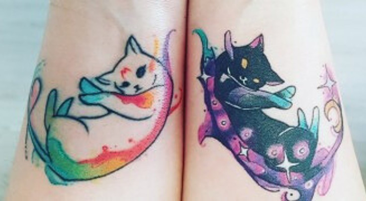 Un gattino stilizzato bianco e uno nero tatuati sul polso di una donna