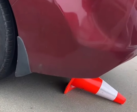 Ein Verkehrskegel wird unter das Auto geklemmt