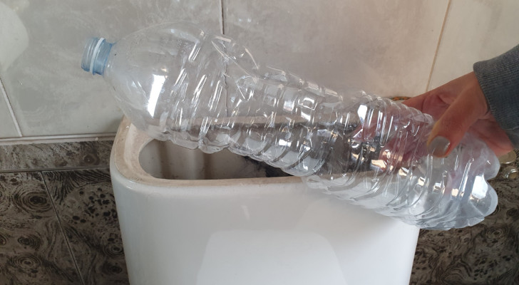 Een plastic fles in de hand bij het reservoir van een toilet
