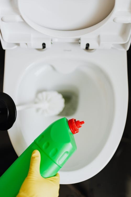 Een persoon maakt een toilet met een wc-borstel en een specifiek schoonmaakmiddel schoon