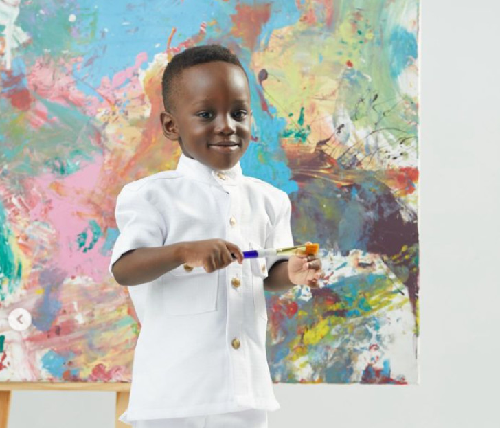 's Werelds jongste kunstenaar, Ace-Liam Ankrah, poseert met een penseel in zijn hand voor een van zijn schilderijen