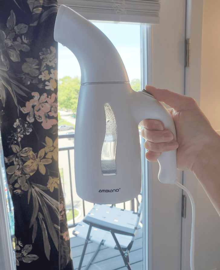 a hand-held vertical steam iron being used on a curtain