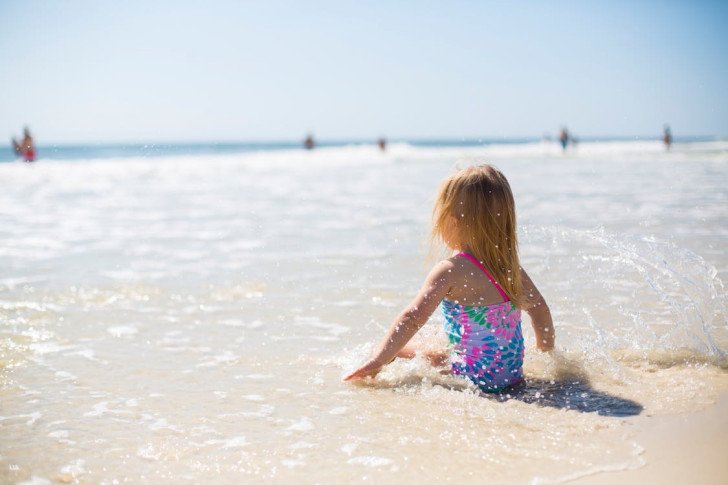 a little girl in a bathing suit sitting in the surf