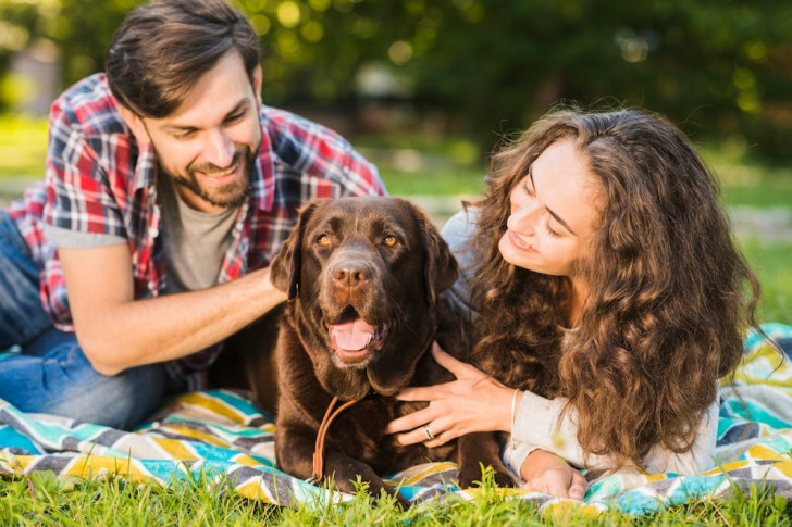 una coppia sorridente stesa su un prato mentre accarezza un cane