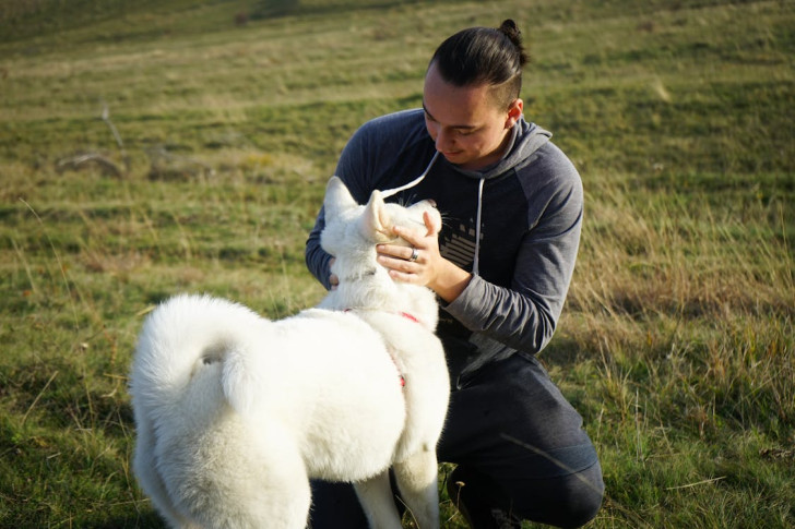 un ragazzo inginocchiato su un prato guarda il cane negli occhi con affetto mentre tiene il suo muso tra le mani