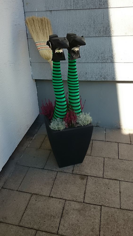 a witch's legs sprouting from a flower pot at the entrance to the house