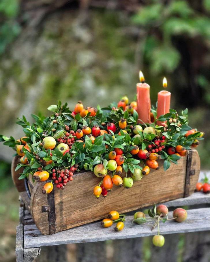 Petite caisse en bois décorée avec des branches de conifères, des bougies et des baies rouges et oranges