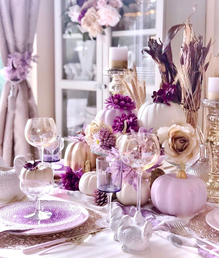 Un grand centre de table dans les tons blanc et violet avec des citrouilles et des pommes de pin