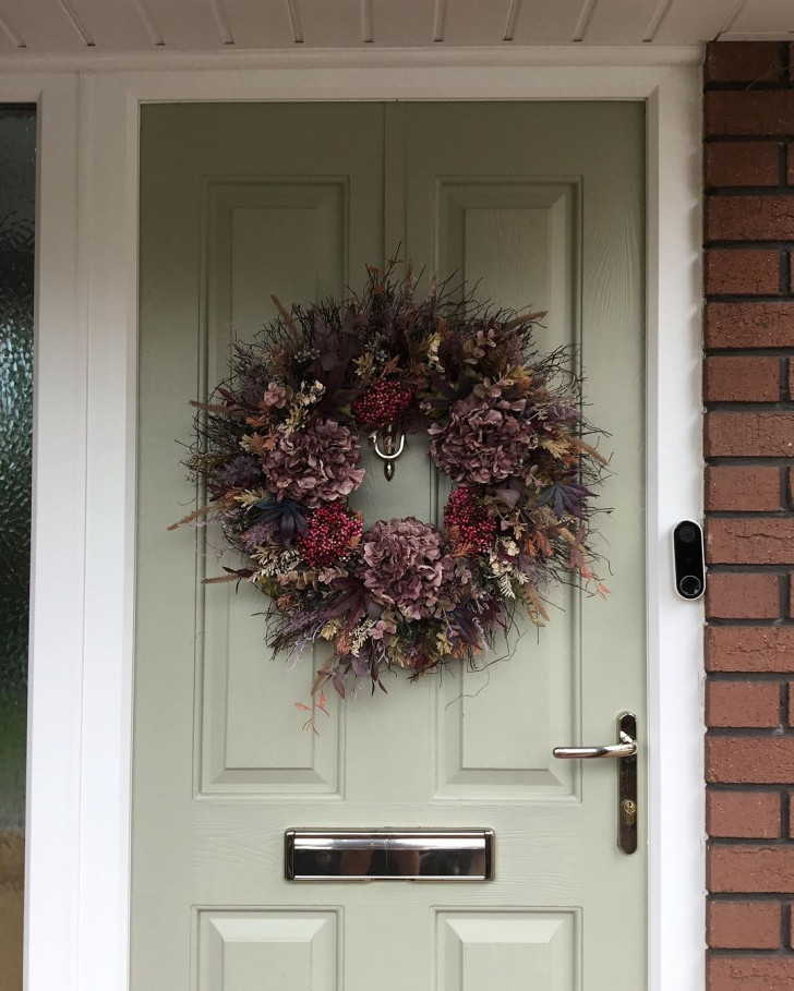 An autumnal door wreath with leaves in shades of red and brown, dried flowers, ears of corn and small red berries.